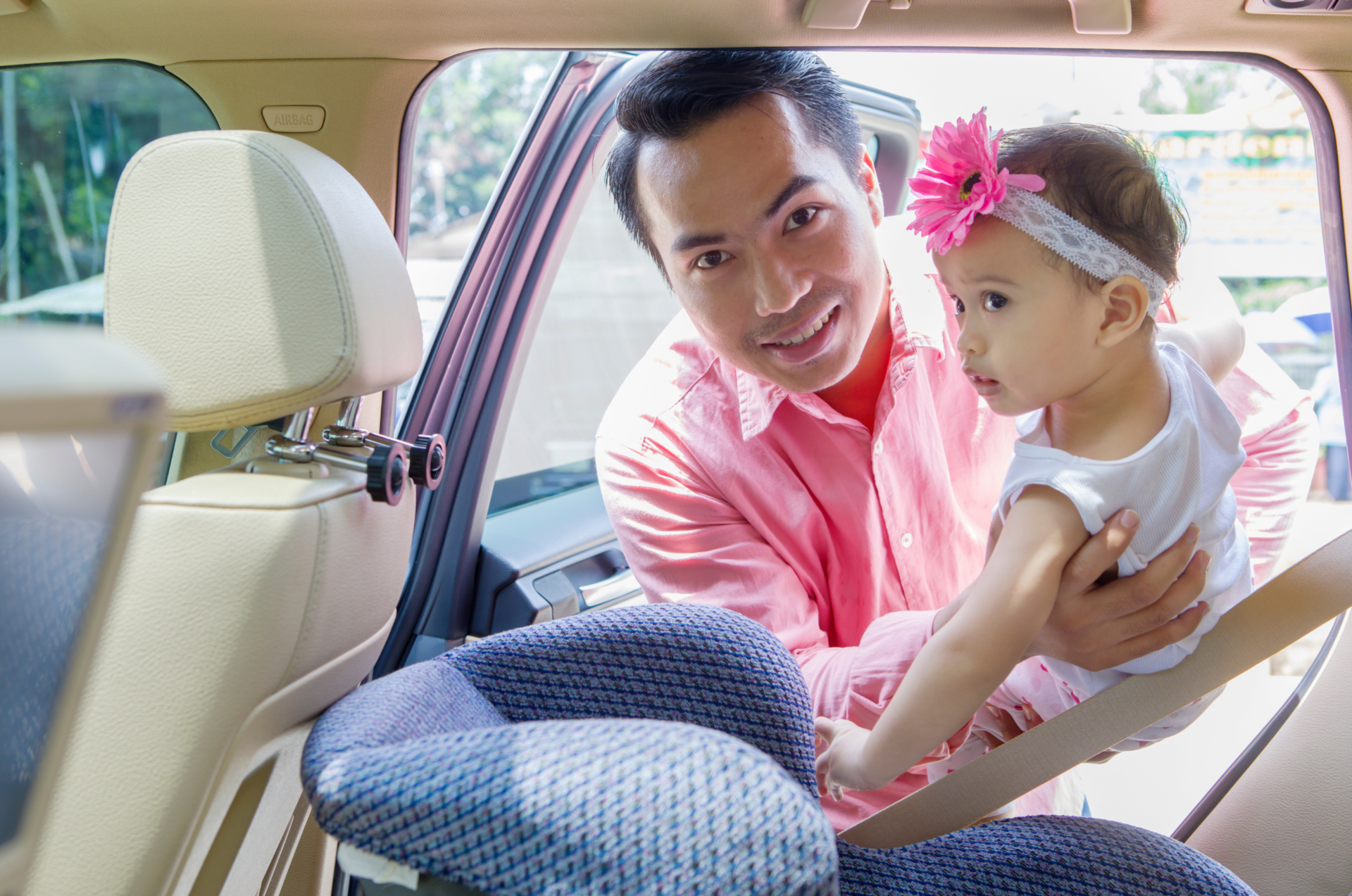 Caregiver putting a preschooler into a rear-facing car seat in the back seat of a vehicle.